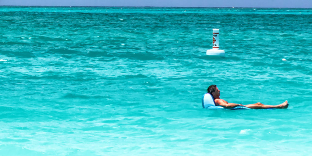 Photo of Billy McFarland floating on an inflatable recliner drifts in a turquoise blue ocean